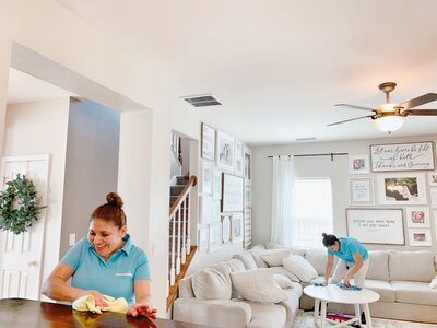 Two Merry Maids professionals cleaning a dining room table and coffee table